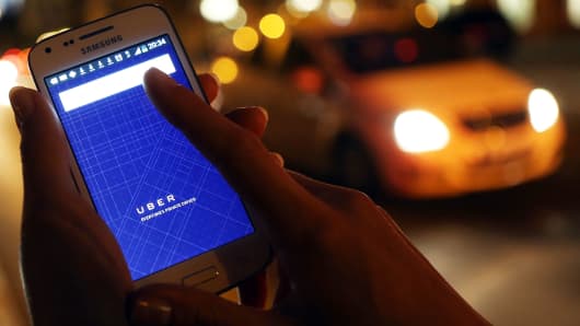 A woman uses the Uber app on a smartphone as a taxi cab drives by.