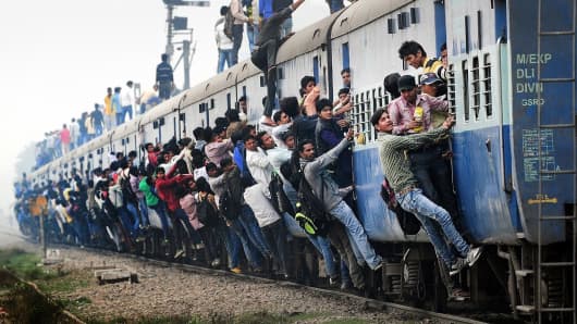 Indian passengers stand and hang onto a train as it departs from a station on the outskirts of New Delhi.