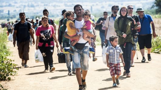 A man carries two children as he walks with other migrants near the southern Serbian village of Miratovac, travelling on foot from Macedonia to Presevo in Serbia, on August 25, 2015. At least 2,000 more migrants flooded overnight into Serbia in a desperate journey to try and go on to Hungary, the door into the European Union, a UN official said on August 24. More than 9,000 people, mostly Syrian refugees, have arrived to Serbia those last three days.