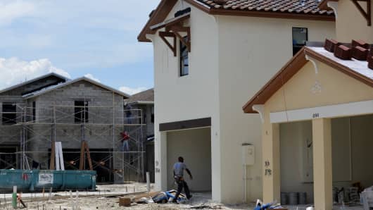 Plasterers stand on scaffolding, back, while a worker walks into the garage of a home under construction at the Lennar Corp. Madison Pointe at Central Park development in Doral, Florida.
