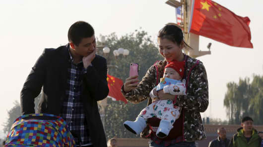 A couple takes pictures with their baby on the Tiananmen Gate in Beijing November 2, 2015. China must continue to enforce its one-child policy until new rules allowing all couples to have two children go into effect, the top family planning body said.
