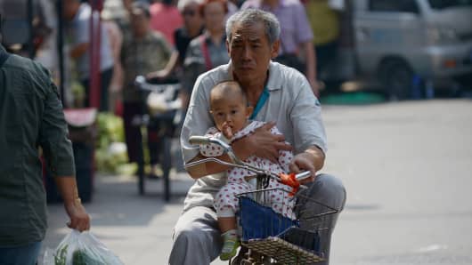 An elderly man holds a baby in his arms as he rides a bicycle along a road in Beijing on September 8, 2015.