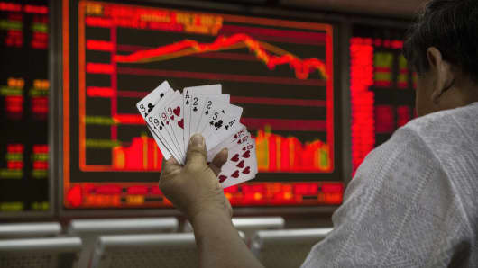 A Chinese day trader plays cards wit5h others as he watches a stock ticker at a local brokerage house in Beijing, China.
