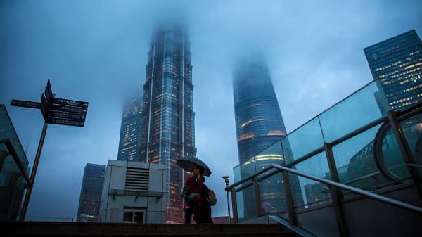 Pedestrians holding an umbrella walk as buildings stand shrouded in haze in the Lujiazui district of Shanghai, China.