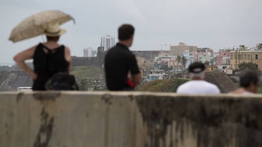 Tourists take a break after visiting the El Morro fort, where part of Old San Juan, Puerto Rico, is visible.