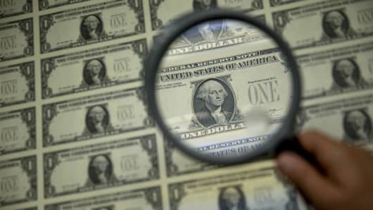 A magnifying glass is held over a 50 subject one dollar note sheet after being printed by an intaglio printing press