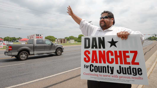 Candidate Dan Sanchez waves at passing vehicles as he campaigns outside of Burns Elementary, May 24, 2016, in Brownsville, Texas.
