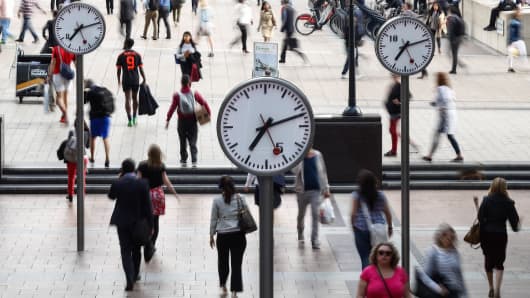 Pedestrians walk past clocks in the Canary Wharf financial, shopping and business district in London, U.K., on Tuesday, June 21, 2016. 