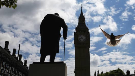 A pigeon flies past a statue of Winston Churchill and the Houses of Parliament in London.
