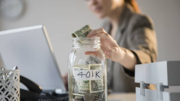 Businesswoman putting money into 401K jar at desk