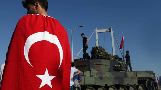 People gather for celebration around Turkish police officers, loyal to the government, standing atop tanks abandoned by Turkish army officers, against a backdrop of Istanbul's iconic Bosporus Bridge in Istanbul, July 16, 2016, Turkey.
