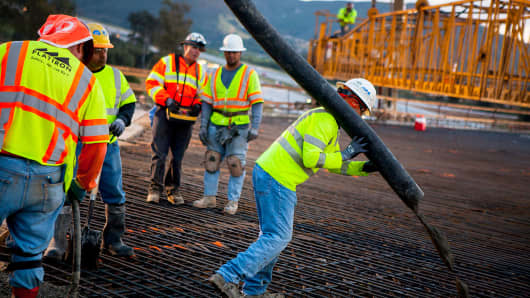 Construction workers pour concrete as part of a bridge expansion project in California.