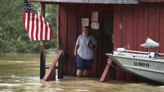 A person is seen on the front porch of a home as it is surrounded by flood waters on August 16, 2016 in Port Vincent, Louisiana.