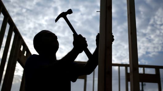 The silhouette of a contractor is seen hammering wood framing for a house under construction in the Norton Commons subdivision of Louisville, Kentucky.