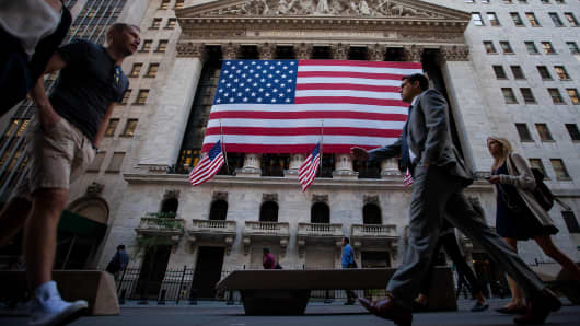 Pedestrians walk past an American flag displayed outside of the New York Stock Exchange (NYSE) in New York.