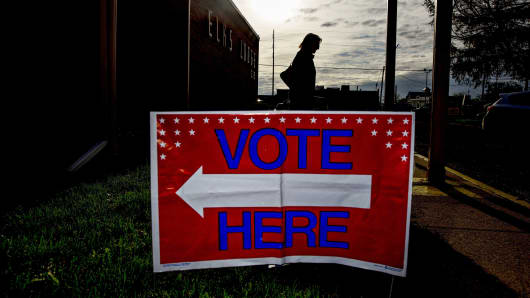 A 'Vote Here' sign stands as the silhouette of a resident is seen exiting a polling station