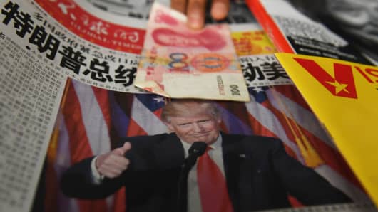 A vendor picks up a 100-yuan note above a newspaper featuring a photo of U.S. President-elect Donald Trump, at a newsstand in Beijing on November 10, 2016.