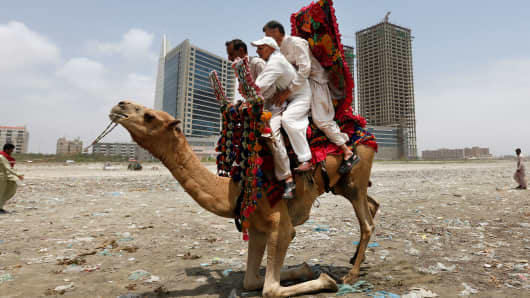 Men sit on a camel as they prepare to take a ride along Clifton beach in Karachi, Pakistan.