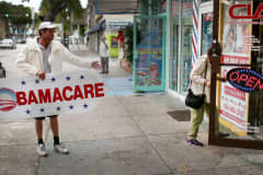 In this 2015 file photo, a man holds a sign directing people to an insurance company where they can sign up for the Affordable Care Act.