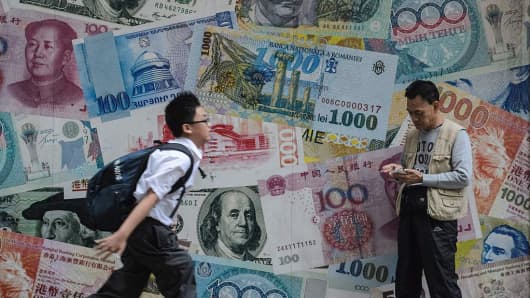 A student runs past a man checking his phone in front of a display showing bank notes of different currencies in Hong Kong on November 9, 2016.