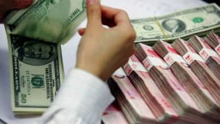 A bank teller counts the stack of Chinese yuan and US dollars at a bank in Shanghai.