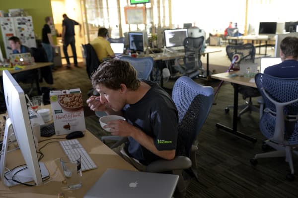 Twenty-seven-year-old Garston Tremblay, a developer, enjoys a bowl of cereal at his desk while at work at Rally Software Development.