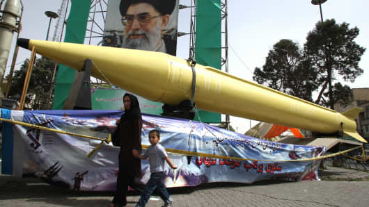An Iranian woman and her son walk past Shahab-2 (L) and Shahab-3 missiles on display in front of a large portrait of Iran's Supreme Leader Ayatollah Ali Khamenei in a square in south Tehran.