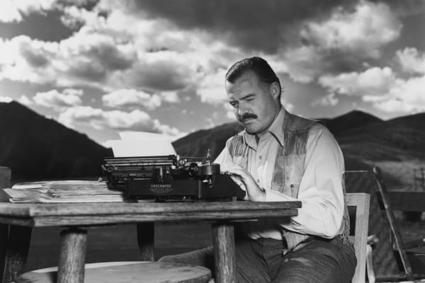 American writer Ernest Hemingway (1899 - 1961) works at his typewriter while sitting outdoors, Idaho. Hemingway disapproved of this photograph saying, 'I don't work like this.'
