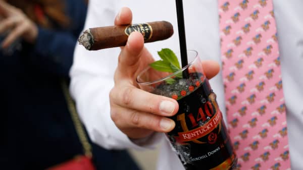 A racegoer holds a cigar and Mint Julep cocktail in the infield at Churchill Downs on the eve of the Kentucky Derby in Louisville, Kentucky.
