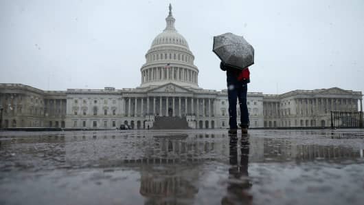 A person takes cover under an umbrella while snapping a photo of the U.S. Capitol in Washington, DC.