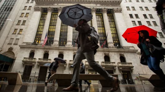 Pedestrians with umbrellas pass in front of the New York Stock Exchange