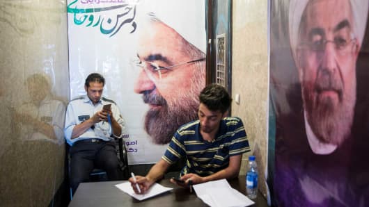 Men use their smartphones to follow election news as posters of Iran's President Hassan Rouhani are seen in Tehran, Iran May 17, 2017.