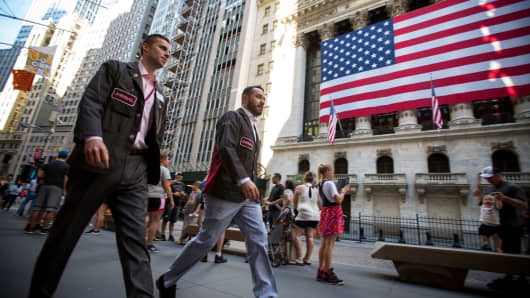 Traders pass in front of an American flag displayed outside of the New York Stock Exchange in New York.