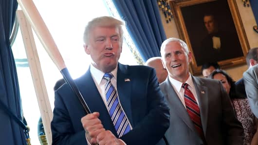 Vice President Mike Pence laughs as President Donald Trump holds a baseball bat. Trump promised he would take more legal and regulatory steps during the next six months to protect American manufacturers, lashing out against trade deals and trade practices he said have hurt U.S. companies.