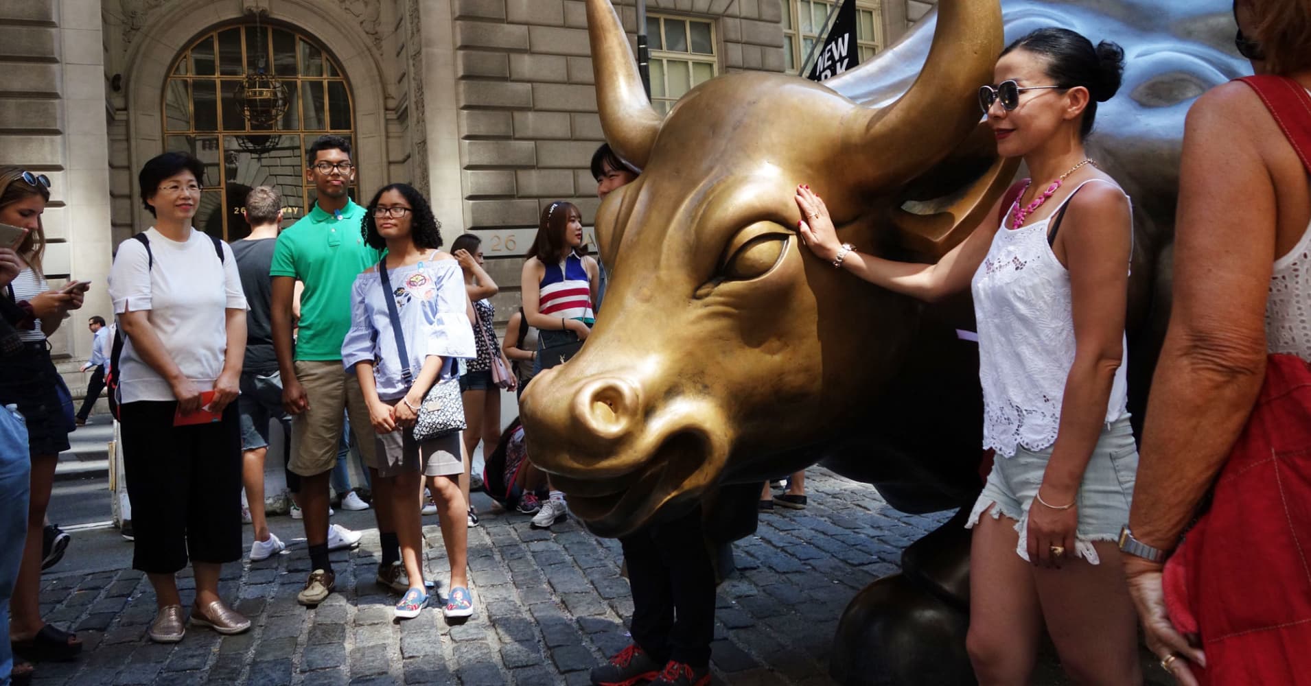 Tourists pose for a picture with the bull sculpture near Wall Street in New York,