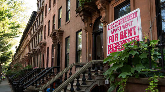 A sign advertises an apartment for rent along a row of brownstone townhouses in Brooklyn, New York.