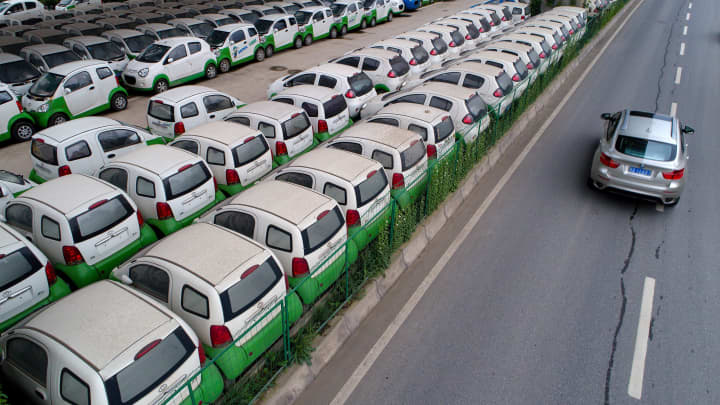 This photo taken on May 22, 2017 shows a car passing new electric vehicles parked in a parking lot under a viaduct in Wuhan, central China's Hubei province.