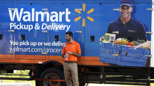 A Walmart Pickup-Grocery employee waits next to a truck.