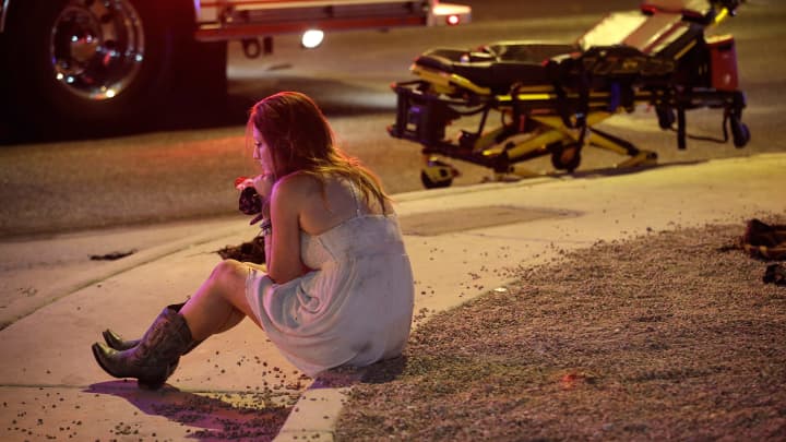 A woman sits on a curb at the scene of a shooting outside of a music festival along the Las Vegas Strip, Monday, Oct. 2, 2017, in Las Vegas. Multiple victims were being transported to hospitals after a shooting late Sunday at a music festival on the Las Vegas Strip.