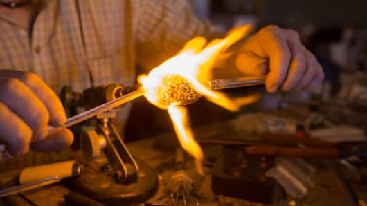 A glassblower working with a torch making small scale pipes and ornaments.