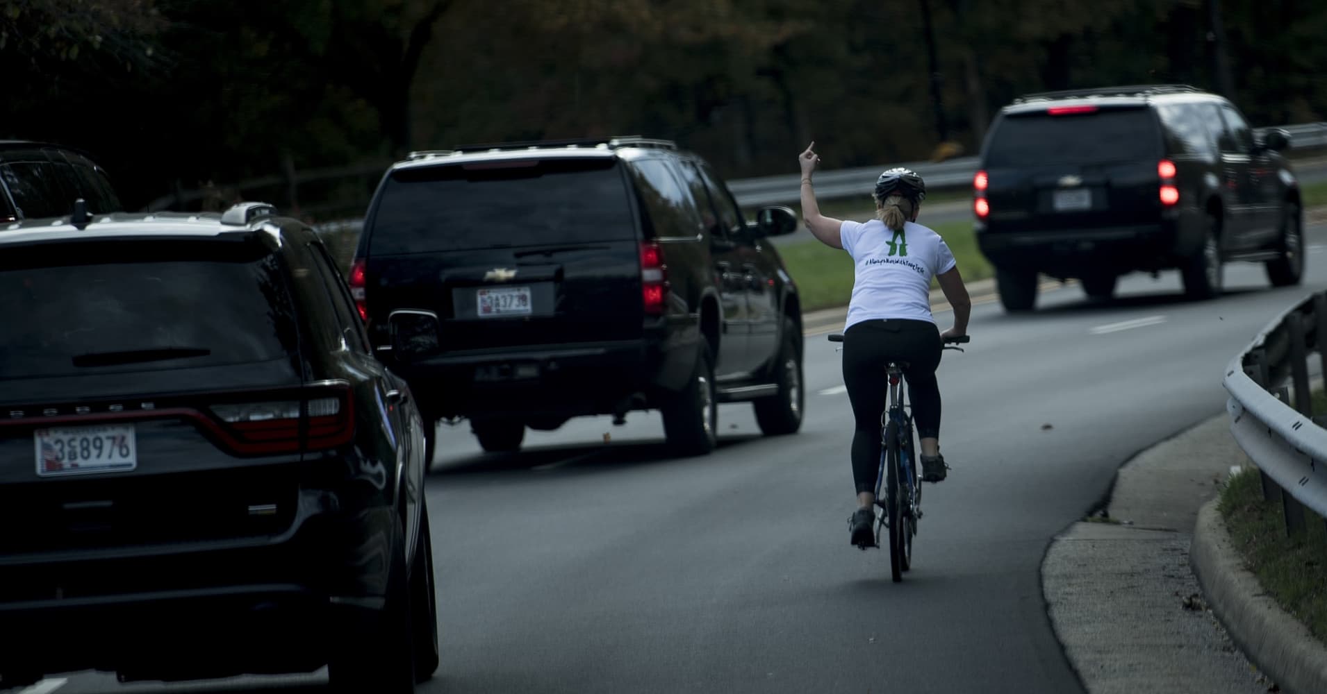 A woman on a bike gestures with her middle finger as a motorcade with US President Donald Trump departs Trump National Golf Course October 28, 2017 in Sterling, Virginia.