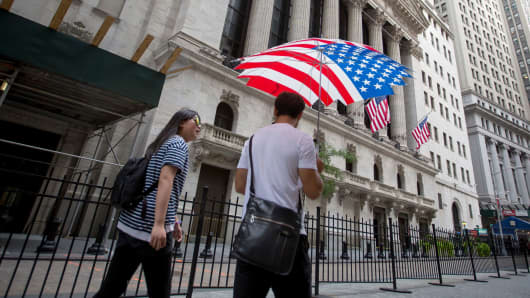 Pedestrians carrying an American flag umbrella pass in front of the New York Stock Exchange.