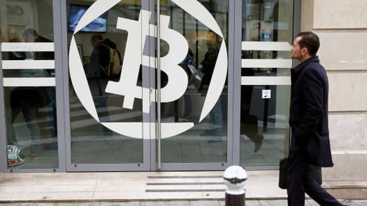 A man walks past a Bitcoin symbol on a window of the offices of the bank 'La Maison du Bitcoin' in Paris.