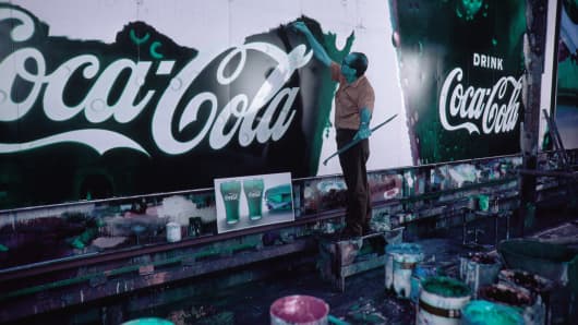 A graphic artist paints a Coca-Cola billboard.