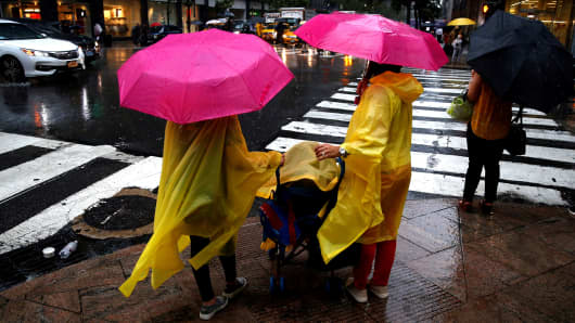 People walk over a pedestrian crossing with their umbrellas on a rainy day in New York, United States on July 17, 2018. 