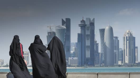 Three Arab women wearing traditional abaya watching the futuristic skyline of Doha, Qatar.