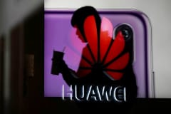 A man walking past a Huawei P20 smartphone advertisement is reflected in a glass door in front of a Huawei logo, at a shopping mall in Shanghai, China December 6, 2018. 