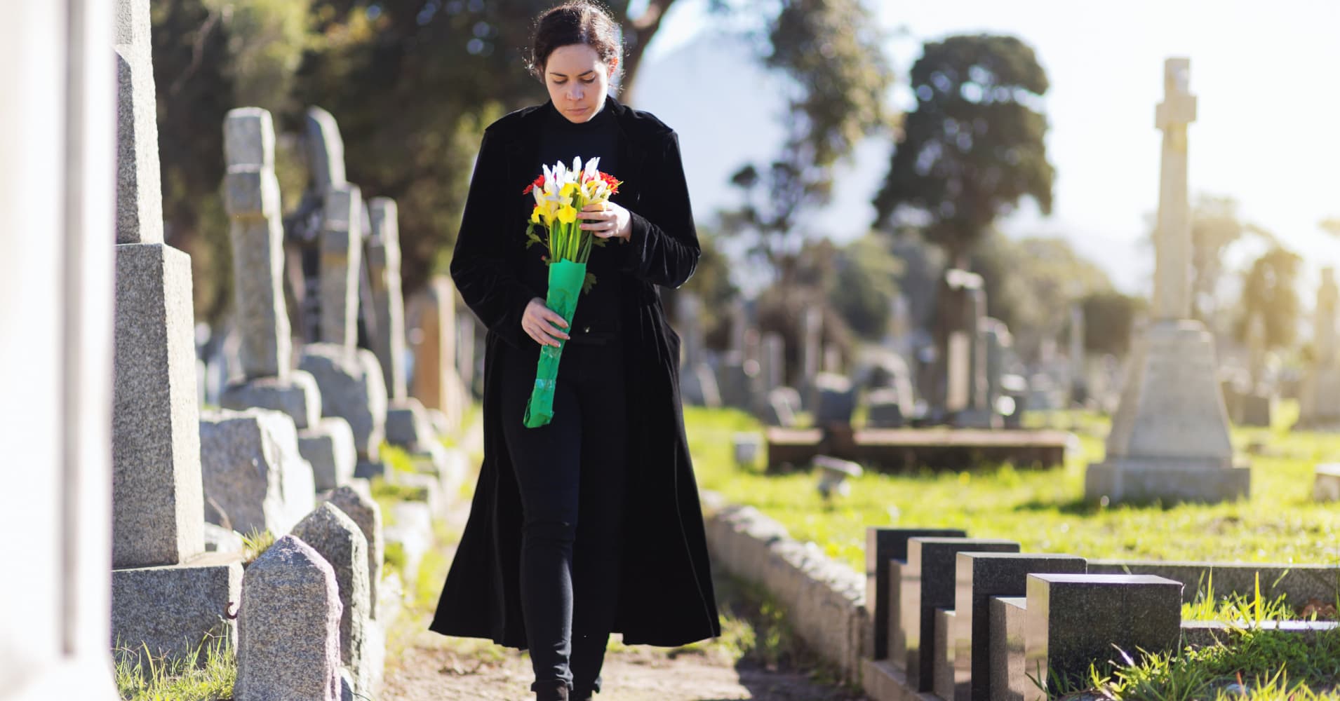 Bereaved young woman in black taking flowers to grave
