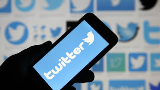 In this photo illustration the Twitter logo is displayed on the screen of an iPhone in front of a computer screen displaying Twitter logos.