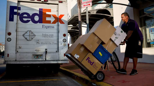 A driver pushes a dolly of boxes to load onto a FedEx delivery truck in Miami.